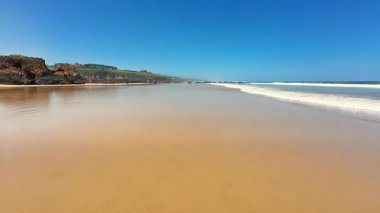 Yumuşak, sıcak kum, hafif dalgalar ve berrak mavi gökyüzü ile işaretlenmiş resim gibi ve sakin bir sahil sahnesi.