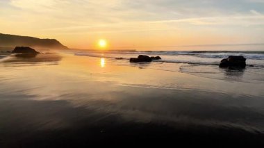 Huzurlu ve sakin bir sahil günbatımı, yumuşak dalgalar sergiliyor kayalık kıyı şeridine hafifçe çarpıyor