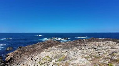 Engebeli kayalık kıyı şeridinin nefes kesici manzarası berrak, güzel mavi gökyüzünün altında engin okyanusla buluşuyor.