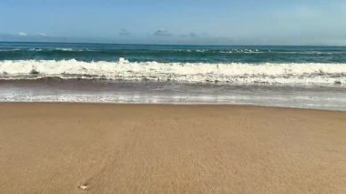 Huzurlu ve sakin bir sahil, parlak beyaz kumların üzerinde, açık mavi gökyüzünün altında yavaşça yuvarlanan altın dalgaları barındırır.