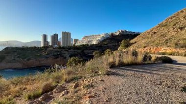 Huzurlu bir kıyı şeridine bakan güzel ve pitoresk bir çakıl yolu. Arka planda modern binalar var.