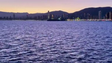 Huzurlu bir akşam sahnesi güzel bir günbatımı sergiliyor. Arka planda şehrin ufuk çizgisi var..