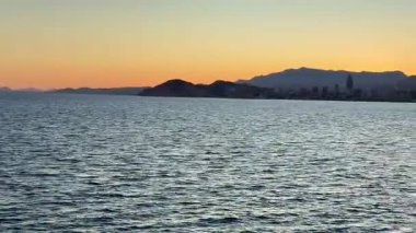 Nefes kesici bir günbatımı, arka planda çarpıcı bir silueti olan sakin suya güzel bir şekilde yansıyor.