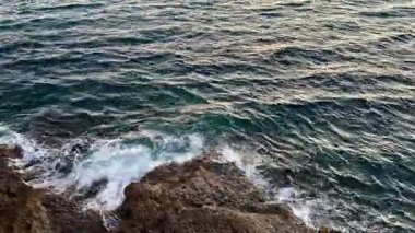 Huzurlu bir okyanus manzarası yumuşak dalgalar ve kayalık bir sahil şeridinde büyüleyici bir gün batımı.