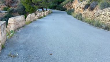 Yeşillik ve kayalık uçurumlarda dolambaçlı bir yol manzarası, doğa aşıkları için mükemmel.