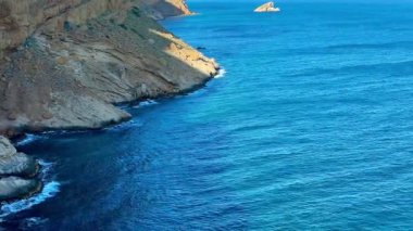 Engebeli kayalıkların sersemletici hava görüntüleri sakin gök mavisi sularla buluşuyor. Resimli bir kıyı manzarası yaratıyor..