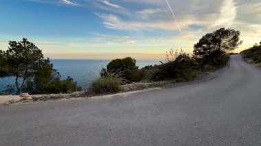 Parlak okyanusun yanındaki sarmal kıyı yolunun çarpıcı manzarası büyüleyici bir gün batımıyla güçlenmiştir.