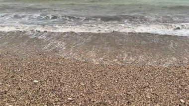 Çakıl taşlı bir kıyı şeridinde nazikçe kopan dalgaların sakin ve resimsel görüntüsü zarafeti güzel bir şekilde yakalıyor.