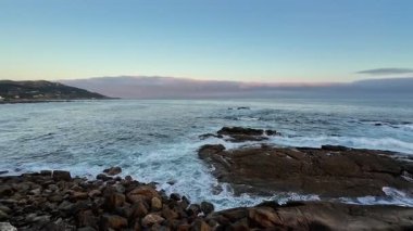 Huzurlu ve huzurlu bir sahil manzarası. Huzurlu bir günbatımı gökyüzünün altında kayalık kıyılara vuran yumuşak dalgaların olduğu.