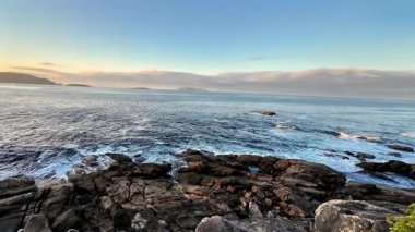 Gün batımında okyanus dalgalarının güçlü bir şekilde kayalık kıyılara çarptığını görmek.