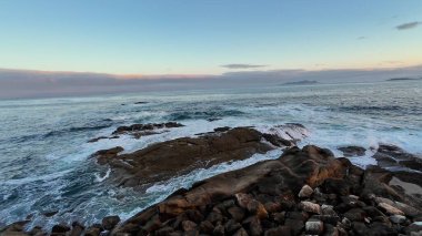 Gün batımında engebeli kayalara hafifçe çarpan okyanus dalgalarının muhteşem sakin ve sakin görüntüsü.