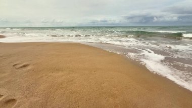 Huzurlu bir sahil sahnesi, sakin dalgalar sergiliyor. Sıcak altın sahilde hafifçe süzülüyor. Rahatlık ve sükuneti davet ediyor.