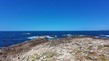 Engebeli kayalık kıyı şeridinin nefes kesici manzarası berrak, güzel mavi gökyüzünün altında engin okyanusla buluşuyor.