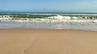 Huzurlu ve sakin bir sahil, parlak beyaz kumların üzerinde, açık mavi gökyüzünün altında yavaşça yuvarlanan altın dalgaları barındırır.
