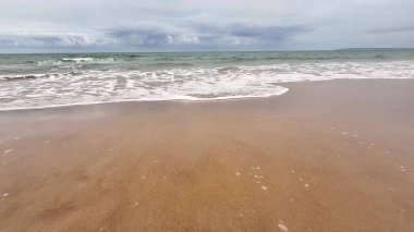 Nazik dalgaların güzel sakin manzarası bulutlu gökyüzünün altındaki altın kumlu kumsalda durmadan süzülüyor.