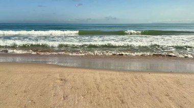 Resmedilmeye değer bir manzara. Yumuşak dalgalar sergiliyor. Güzel kumlu bir kumsalda, berrak mavi bir gökyüzünün altında yavaşça süzülüyor.