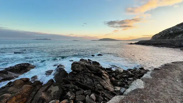 Gün batımında güzel, sakin bir kıyı manzarası, dalgaların ritmik bir şekilde kayalık bir kıyıya çarpması.
