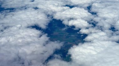 Nefes kesici bir hava perspektifi, yukarıdaki yumuşak, kabarık bulutların arasından süzülen canlı yeşillik gölgeleri sergiliyor.