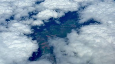 Yumuşak, tüylü beyaz bulutlar tarafından kısmen gizlenmiş uçsuz bucaksız ve yemyeşil bir arazinin nefes kesici hava manzarası.