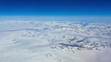 Açık mavi gökyüzünün altındaki kar kaplı dağların büyüleyici güzelliğini vurgulayan nefes kesici bir hava manzarası.