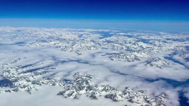 Sersemletici hava görüntüleri, parlak mavi gökyüzü karşısında karla kaplı nefes kesici dağları gösteriyor.