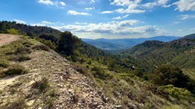 Berrak mavi gökyüzünün altında canlı yeşillikle engin bir dağ manzarasının tadını çıkar.