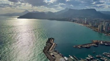 Sersemletici hava manzarası kıyı şehrini, dağları ve bulutlu gökyüzünün altında canlı marinayı gösteriyor..