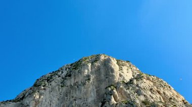 Engebeli, kayalık bir dağın nefes kesici manzarası görkemli, parlak, mavi gökyüzüne karşı duruyor.