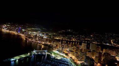 Nefes kesen bir hava manzarası, gece aydınlanan canlı ve canlı bir kıyı şehrini güzel bir şekilde gösteriyor.