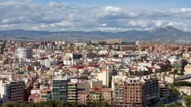 Arka planda yükselen görkemli dağlarla süslenmiş canlı bir şehir manzarasının nefes kesici panoramik görüntüsü.