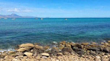 Berrak turkuaz suyu ve parlak güneşin altında hafifçe sallanan tekneleri olan sakin bir deniz manzarası.