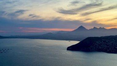 Dağların üzerinde çarpıcı bir günbatımı ve sakin bir deniz hayal gücünü cezbeden pitoresk bir sahil sahnesi yaratır.
