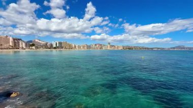 Deniz kenarının nefes kesici manzarası sakin, kristal berrak mavi suların yanındaki binaları sergiliyor.