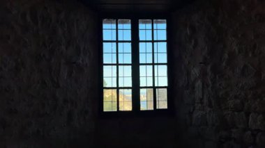Çok güzel hazırlanmış bir pencere çerçevesi tarihi bir taş duvarın ötesindeki doğayı resmediyor.