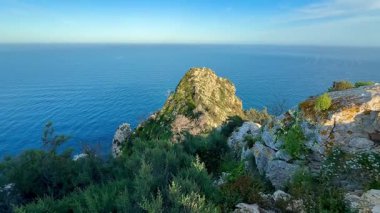 Nefes kesici bir kıyı manzarası dingin ve dingin okyanusa karşı kurulu kayalık kayalıkları canlı bir şekilde gösteriyor.