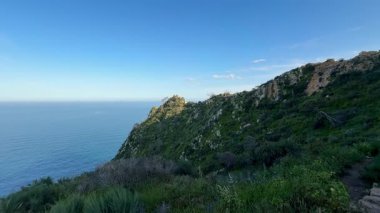 Görkemli uçurumların, canlı yeşilliğin ve sakin okyanus sükunetinin yer aldığı nefes kesici güzellikte bir kıyı manzarası.