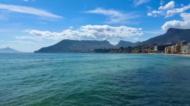 Göz kamaştırıcı kıyı manzarası temiz su, görkemli dağlar ve arka planda kumlu plajlar içerir.