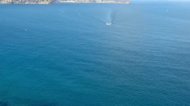 Bu çarpıcı hava fotoğrafı sakin okyanus dalgalarını ve güzel bir kıyı manzarasının yakınındaki bir tekneyi yakalar.