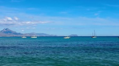 Açık mavi gökyüzü altında zarifçe süzülen çeşitli teknelerin yer aldığı fevkalade bir deniz manzarası.