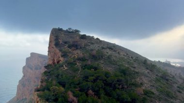 Bereketli yeşillikler ve çarpan okyanus dalgalarıyla çevrili sarp bir uçurumun çarpıcı hava manzarasını deneyimleyin.