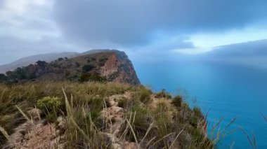 Bulutlu bir gökyüzünün altındaki parlak gök mavisi suların üzerindeki kıyı uçurumunun nefes kesici ve çarpıcı görüntüsü.