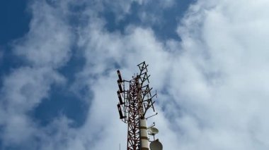 Görüntü, bir telekom kulesini kabarık bulutlu parlak mavi bir gökyüzüne doğru gösteriyor.