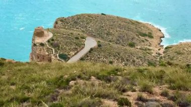 Dalgalı mavi denizin kıyısındaki kayalık arazide dolambaçlı bir yolda yürürken çarpıcı sahil manzarasının tadını çıkar.