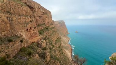 Bulutlu bir günde dingin mavi bir okyanusun yanında duran engebeli uçurumların nefes kesici manzarası.