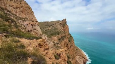 Bulutlu bir gökyüzünün altında dramatik uçurumlara mükemmel bir şekilde kurulmuş canlı turkuaz suların çarpıcı manzarasını deneyimleyin.