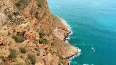 Nefes kesici uçurumlar dramatik bir şekilde yükselir, sakin turkuaz okyanus dalgalarıyla karşılaşır bulutlu bir gökyüzünün altında usulca yuvarlanır