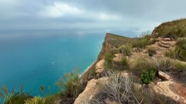 Şaşırtıcı güzellikteki manzara bulutlu gökyüzünün altında dalgalı mavi bir okyanusla engebeli bir uçurum kenarı sergiliyor.