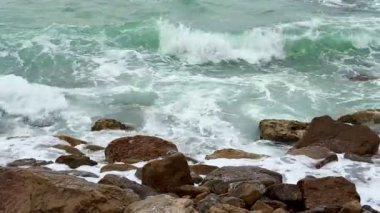 Huzurlu, nazik dalgalar engebeli kıyı kayalarını tekrar tekrar silip süpürüyor. Güzel, sakin bir deniz manzarası.