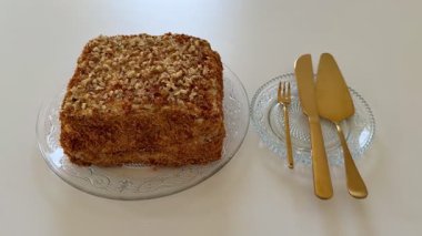 Zarif bir şekilde sunulmuş kare bir pasta, üzerinde çeşitli fındıklar var, eski cam bir tabakta.