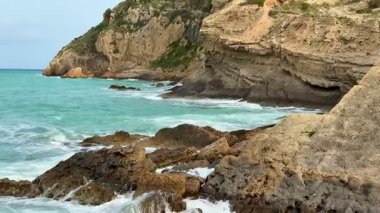 Kristal berrak mavi deniz dalgalarıyla birlikte engebeli kayaları barındıran nefes kesici bir kıyı manzarası keşfedin.